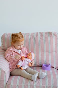 Adorable young girl playing with her baby doll on a comfy striped couch.
