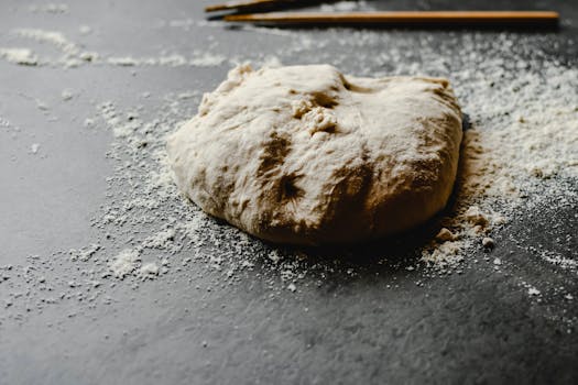 A rustic bread dough placed on a flour-dusted dark surface, perfect for food photography needs.
