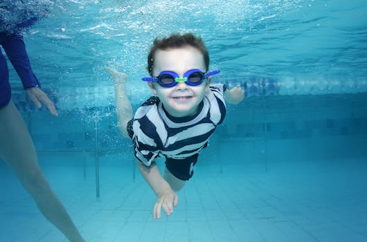 Young boy happily swims underwater in a swimming pool wearing goggles. Summer fun captured.