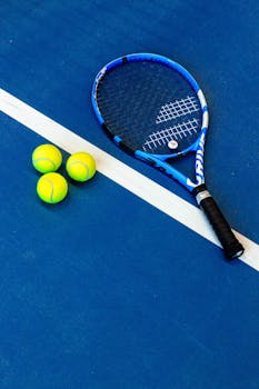 Tennis racket and three balls on a vibrant blue court.
