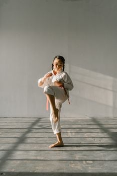A young girl practicing martial arts in a bright, indoor space, showcasing a powerful taekwondo pose.