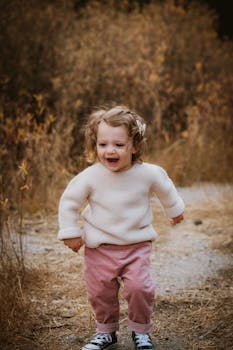 Happy toddler in warm clothes running on a path during fall, showcasing joyful innocence.