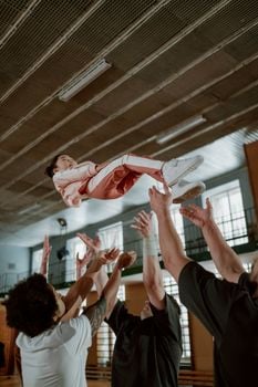 A group of people lifting a girl indoors during an acrobatics practice, capturing teamwork and concentration.