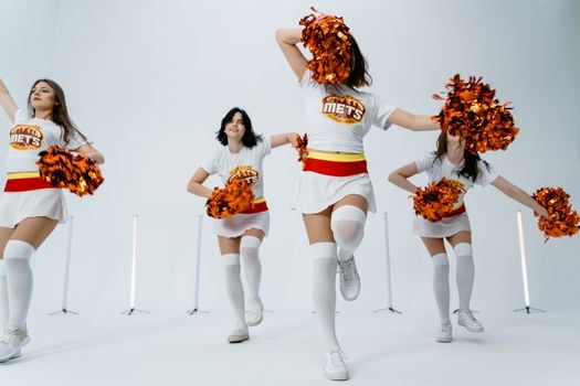 Dynamic group of cheerleaders performing with pom poms in a studio setting.