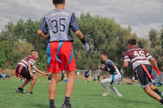 Boys playing flag football on a sunny day in a field, showcasing teamwork.