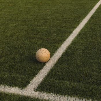 A lone soccer ball rests on a vibrant green field, marked with white lines.