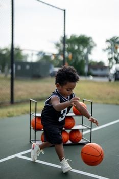 A young child wearing a black jersey plays basketball on an outdoor court, showing energy and focus.