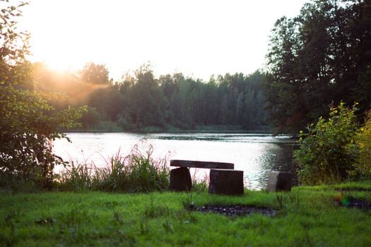 Tranquil photo of a serene lakeside setting at sunrise, featuring a rustic bench.