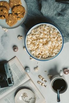 A cozy flat lay featuring popcorn, cookies, black coffee, and a vintage camera.