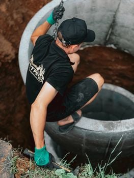 Construction worker installing a concrete well segment outdoors.