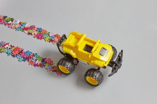 A close-up of a yellow toy truck creating a path with colorful jigsaw puzzle pieces.