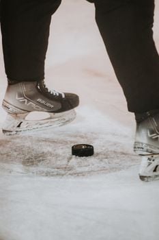 Close-up of ice hockey skates poised above a puck on the rink. Perfect for sports enthusiasts.