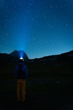 A person stands under a starry night sky using a flashlight, embracing adventure and nature.