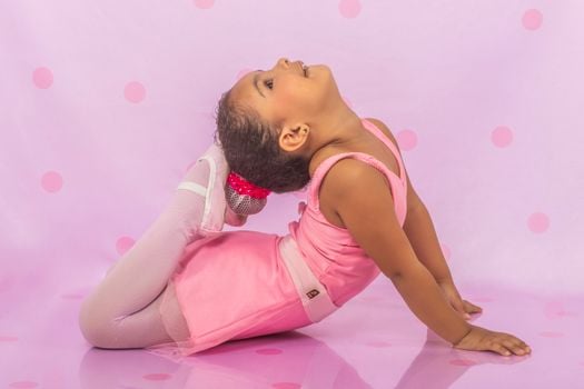 Adorable young girl in a pink ballet outfit performing a graceful dance pose in a studio setting.