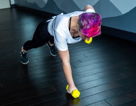 Fit woman in white shirt doing dumbbell exercises indoors, promoting healthy living and fitness.