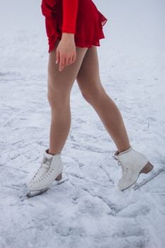 Ice skater wearing a red dress and white skates glides gracefully across the ice.