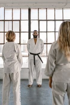 Martial arts instructor and students practicing in a well-lit dojo with large windows.
