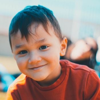 Cute portrait of a young boy smiling warmly outdoors on a sunny day.