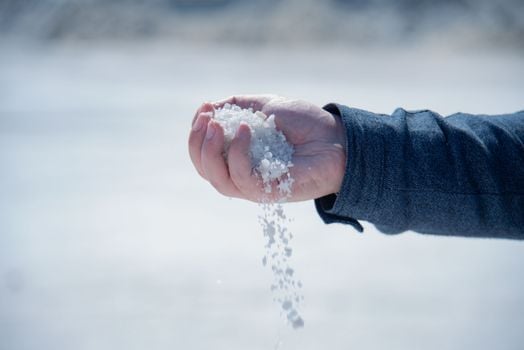 Close-up of a hand holding and pouring coarse white salt outdoors.