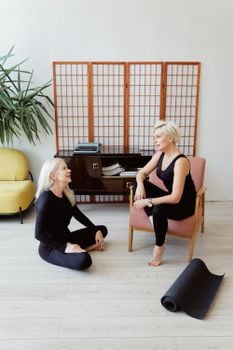 Two women engaging in conversation in a stylish living room with yoga mat and modern decor.