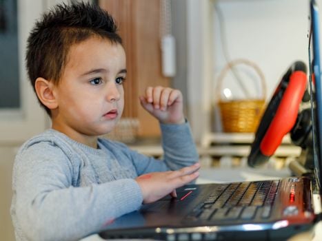 A young child focused on a laptop with a gaming steering wheel setup.