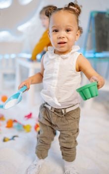 A cheerful child playing indoors with toys, holding sand accessories in hand.
