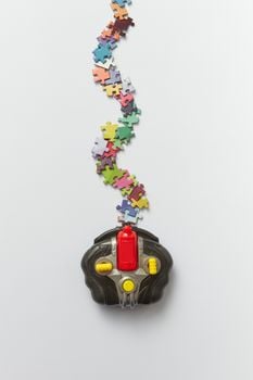 Creative arrangement of colorful puzzle pieces flowing from a toy controller on a plain background.