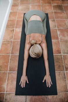 Woman in activewear practicing yoga child's pose on a mat indoors.