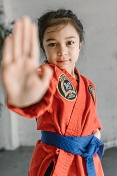A young girl in a karate uniform smiles while practicing a martial arts pose.