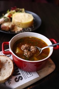 Delicious meatball soup served in a red pot on a wooden board.