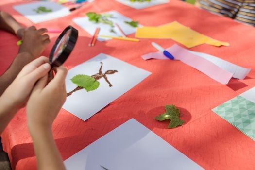 Children engaging in creative crafting with leaves and magnifiers.