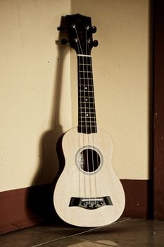 Contemporary acoustic ukulele with light wooden body placed in corner of light room against beige wall