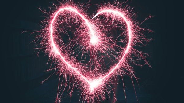 “Pink sparkler forming a heart against a dark background.