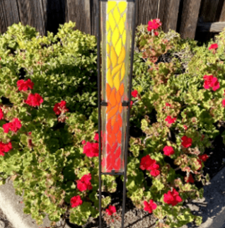 Yellow, orange and red fused glass stake standing in a pot of red flowers. 