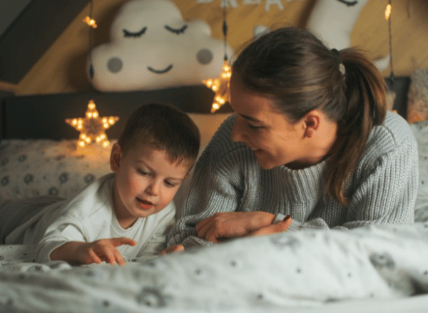 Mother and young boy laying on a bed smiling. Twinkling star lights in the background.