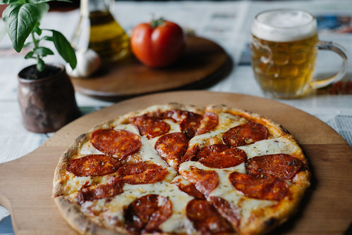 Pizza served on a wooden plate with beer and tomator in the background