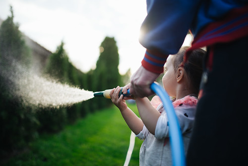 Little girl have fun with water spray in the garden.