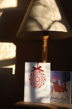 Christmas cards on a wooden table with warm light from a lampshade casting shadows.