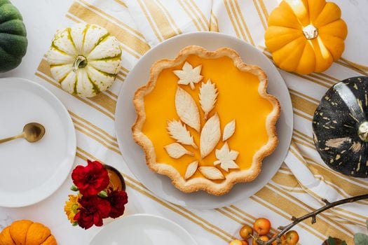 Delicious pumpkin pie with leaf crust design surrounded by gourds and flowers.