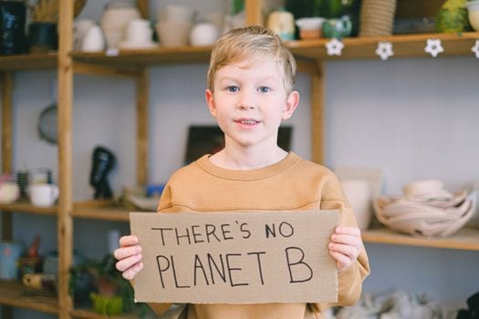 Young boy holding a sign saying 'There's No Planet B,' promoting environmental awareness.