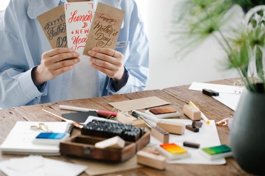 Creative greeting cards held above a messy workspace.