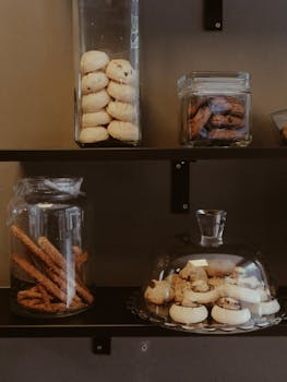Stacked cookies and pastries in clear jars on dark shelves, showcasing a variety of baked goods.