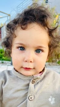 Charming portrait of a curly-haired baby girl with expressive eyes captured outdoors.