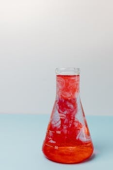 Close-up of a 250 mL glass beaker filled with red liquid in a lab setting.