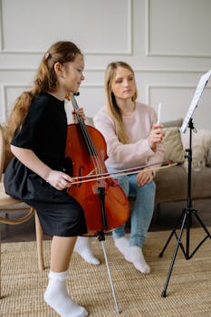 Young girl practicing cello with guidance from music teacher indoors.