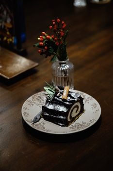 Chocolate yule log cake with powdered sugar and festive decorations on a plate.